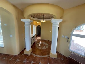A spacious hallway with a tiled floor, a star-patterned tile in the center, and a ceiling fan.