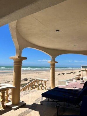 Een overdekt terras met uitzicht op het strand, met een lounge stoel en een balustrade.
