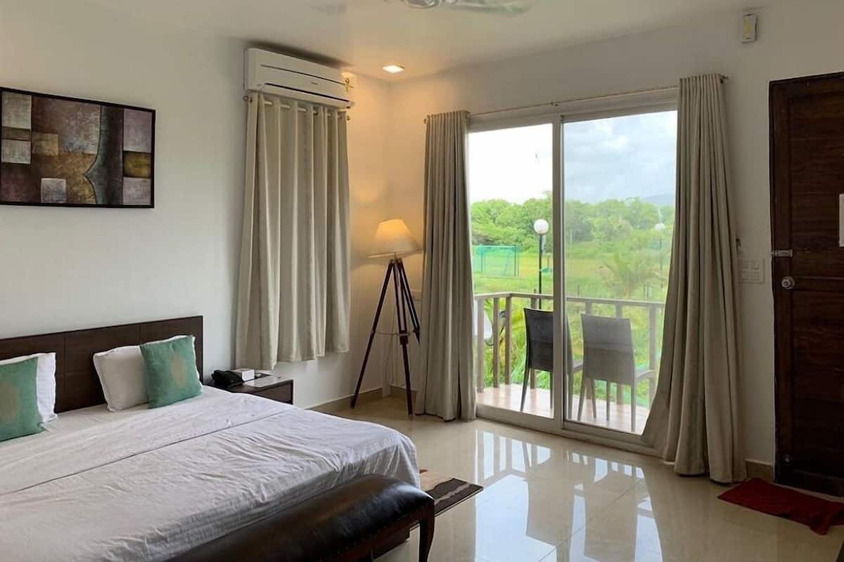 Habitación de hotel con cama, lámpara, cortinas, balcón con sillas y puerta.