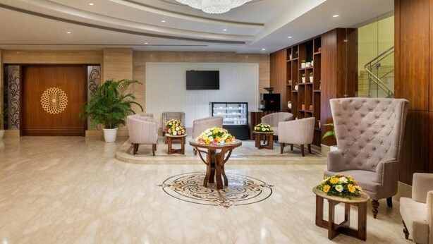 A spacious lobby with a large chandelier, comfortable seating, a reception desk, and a staircase. - Cygnett Inn Paras (Dehradun)