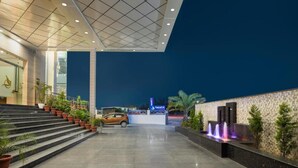 A hotel entrance with a car parked in front, a staircase leading up, and a water feature on the right. - Cygnett Inn Paras (Dehradun)