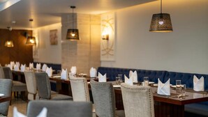 A restaurant with long tables, upholstered chairs, and hanging pendant lights. - Cygnett Inn Paras (Dehradun)
