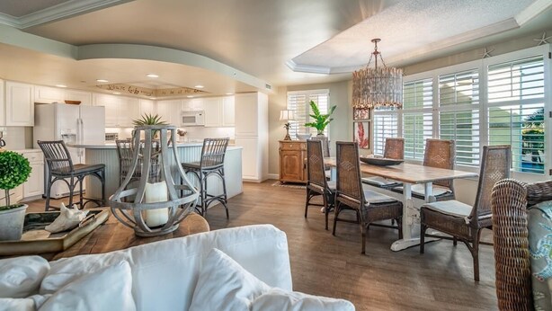 A spacious kitchen with white cabinets, a dining area with wicker chairs, and a large window with blinds. - Ocean Oasis Fordham 101 3BR Villa Ocean Views (Pawleys Island)