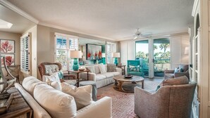 A spacious living room with a large sofa, a coffee table, and a dining area. There is a sliding glass door leading to an outdoor patio. - Ocean Oasis Fordham 101 3BR Villa Ocean Views (Pawleys Island)