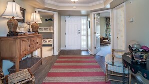 A hallway with a wooden console table, two lamps, a striped rug, wicker chairs, and a door leading to another room. - Ocean Oasis Fordham 101 3BR Villa Ocean Views (Pawleys Island)
