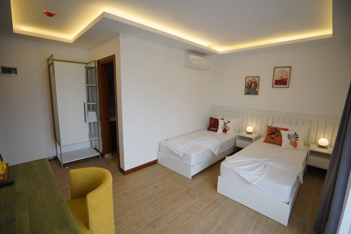 Une chambre d’hôtel avec deux lits simples, un bureau, une chaise et une armoire.