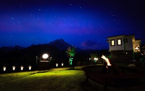 A nighttime view of a mountainous area with a house and a well-lit garden.