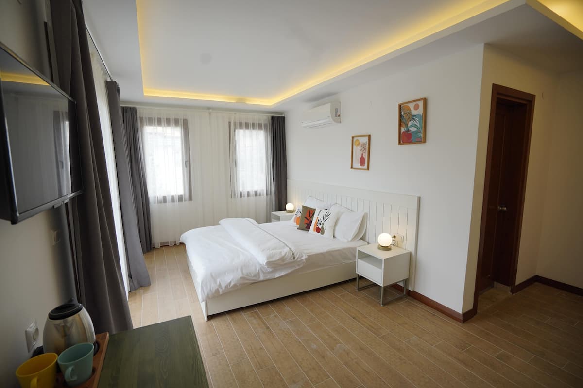 Une chambre d’hôtel moderne dotée d’un grand lit, de tables de chevet, d’un téléviseur à écran plat et d’une fenêtre avec des rideaux.