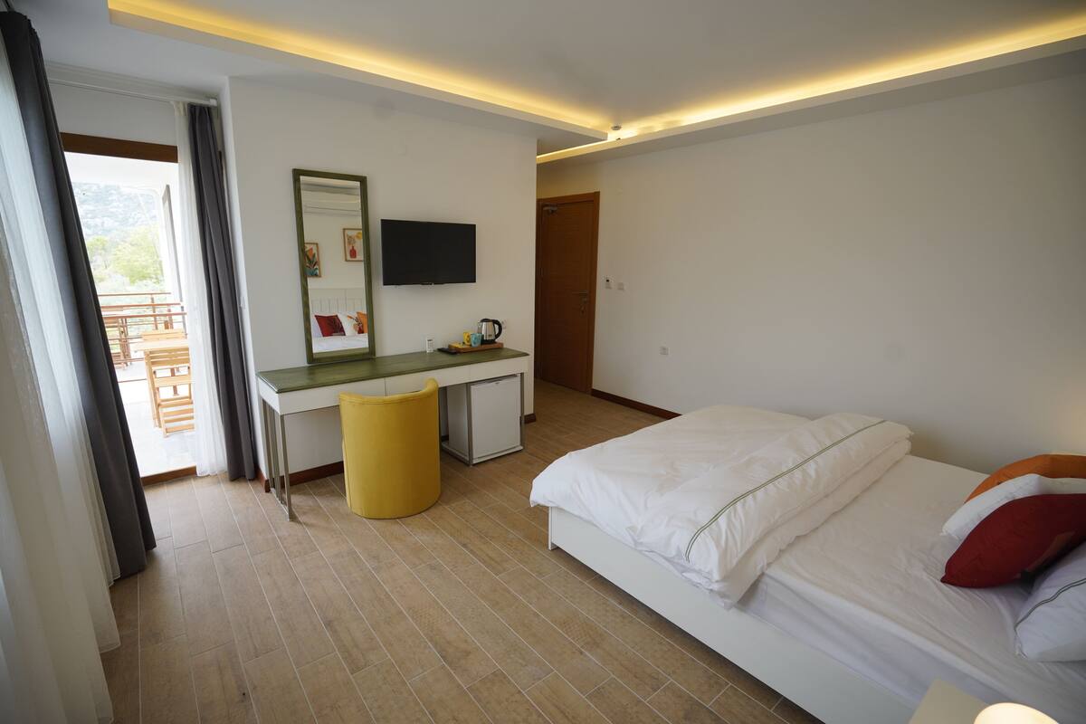 Une chambre à coucher comprenant un lit, un bureau, une chaise, une petite table, un téléviseur et une porte.