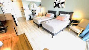 Une chambre d’hôtel avec deux lits, un bureau, une chaise, un miroir et un tableau au mur.