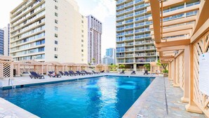 Una piscina con sillones de descanso y una pérgola, rodeada de edificios altos.