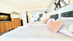 Una habitación de hotel moderna con una cama grande, televisor, armario y espejo.