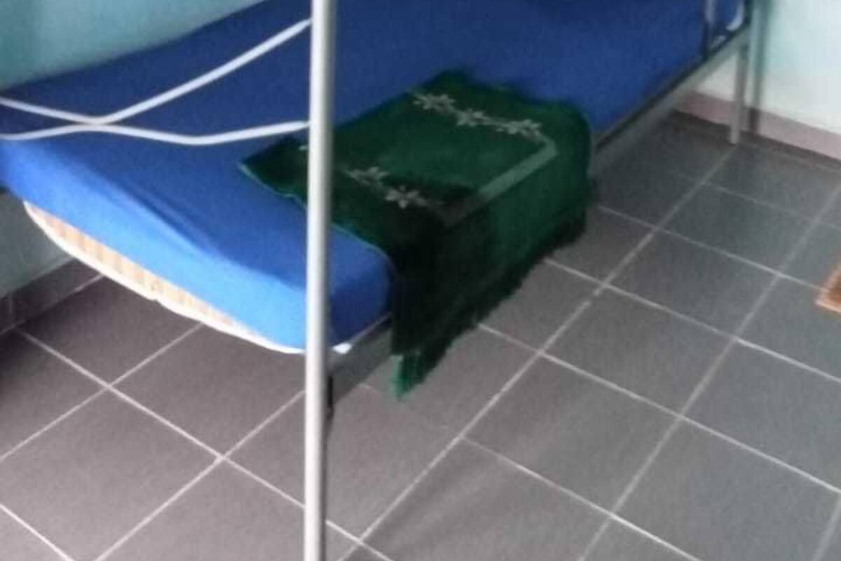Une chambre avec un lit superposé, un matelas bleu, une couverture verte et un climatiseur fixé au mur.