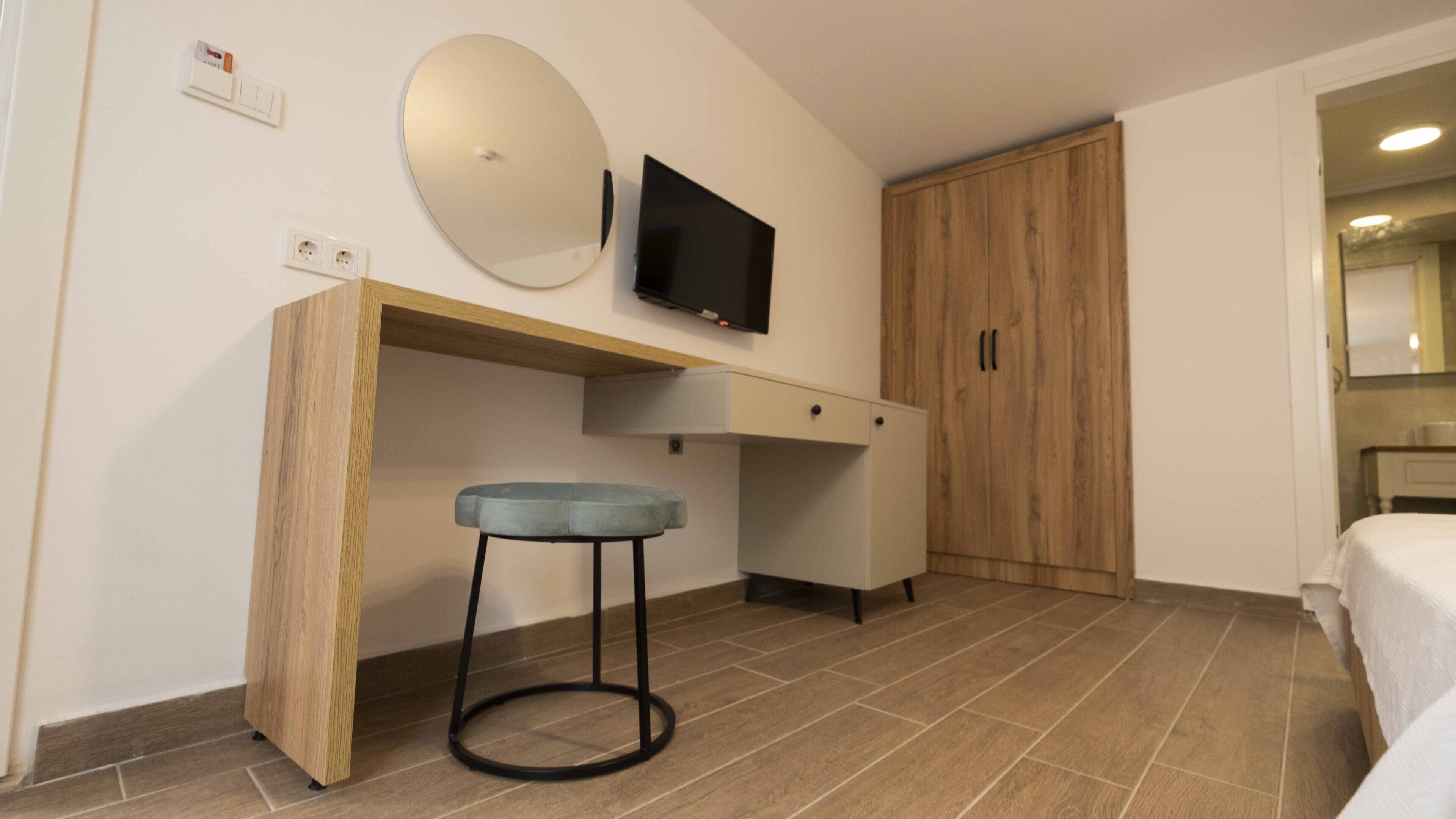A bedroom with a bed, a wooden desk, a chair, a television, and a wardrobe.