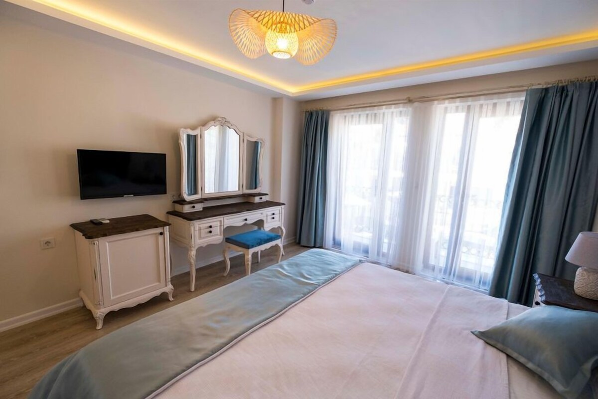 A hotel room with a bed, a television, a dresser, a mirror, and a window with curtains.