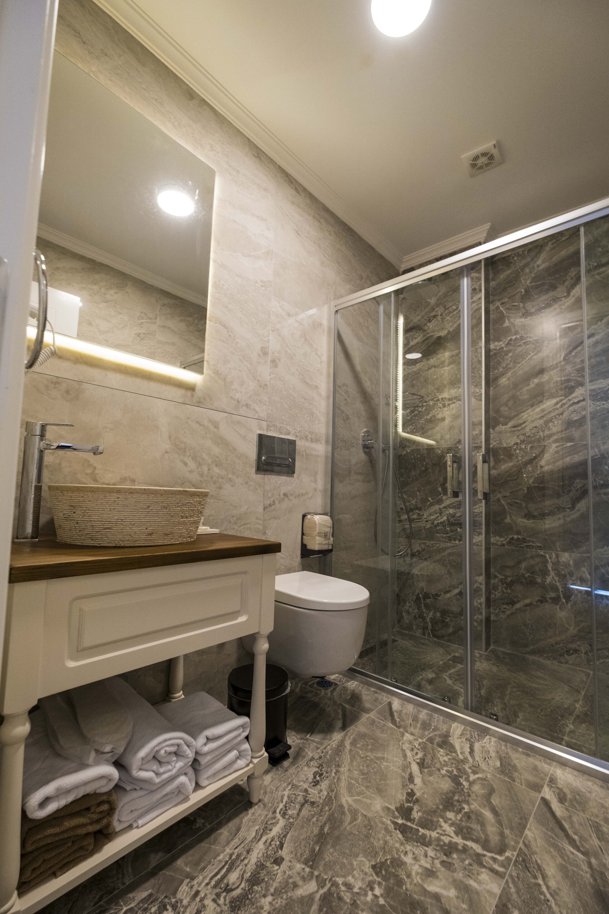 A bathroom with a marble sink, a glass shower enclosure, and a white toilet.