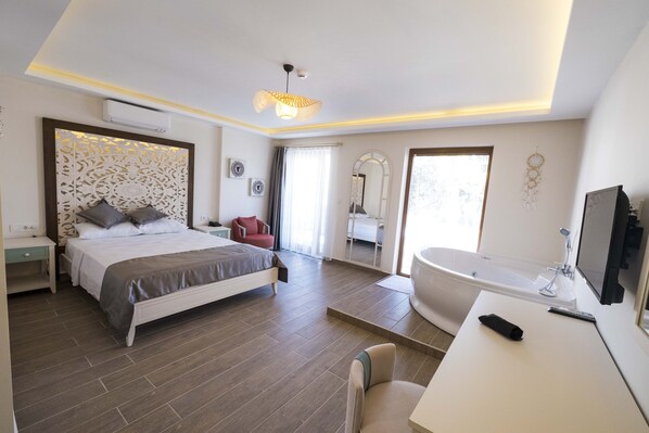 A modern hotel room with a large bed, a separate bathroom with a bathtub, a desk with a remote control, and a decorative wall panel. - ICARUS ALACATI (Cesme)
