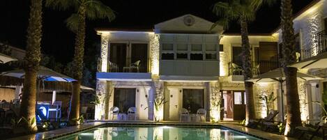 A hotel with a swimming pool, palm trees, and outdoor seating.