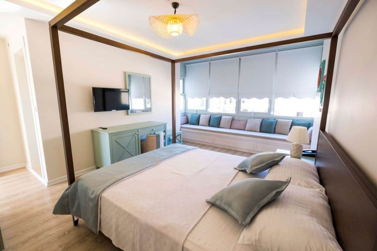 A bedroom with a bed, a TV, a window seat with cushions, and a ceiling light.