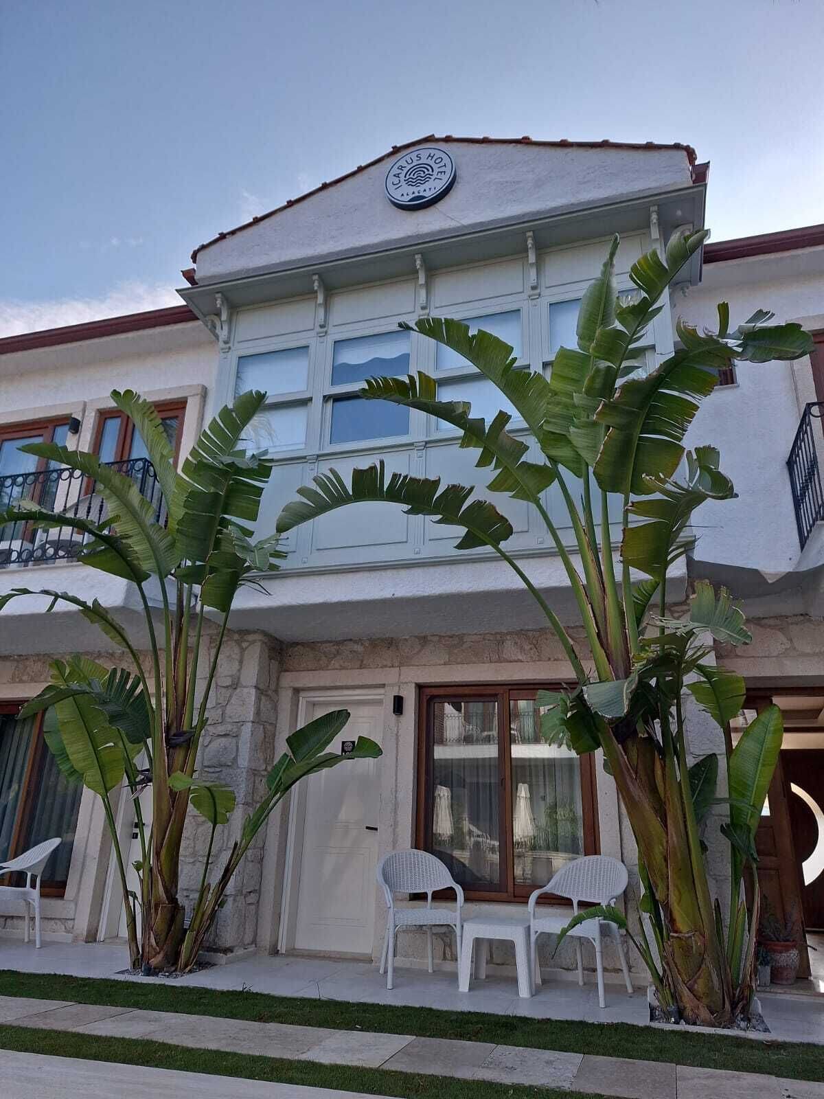 Un hotel con fachada blanca, ventanas grandes y un balcón con sillas.