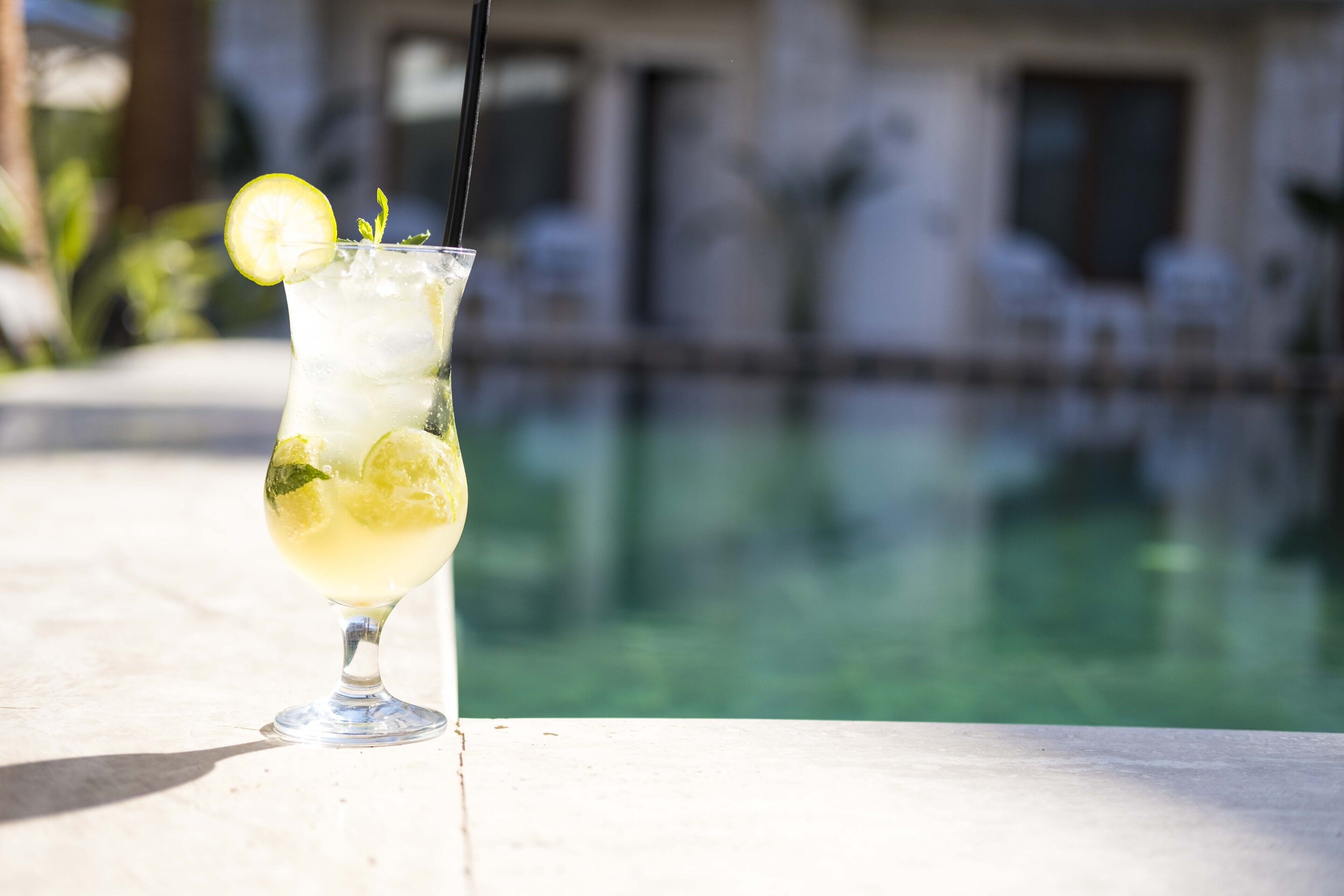 Ein Cocktail mit Zitronenscheibe und Minze, platziert auf einem Tisch am Pool.