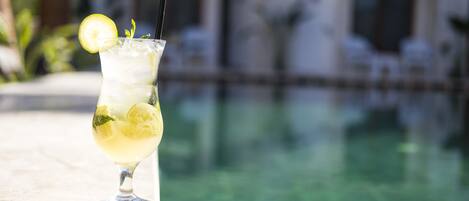 Ein Cocktail mit Zitronenscheibe und Minze, platziert auf einem Tisch am Pool.