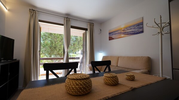A modern room with a sofa, two chairs, a TV, and a painting of a sunset.
