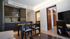 A modern kitchen with dark wood cabinets, a built-in microwave, and a black countertop. There is a dining area with a wooden table and chairs, and a black entertainment unit with books.