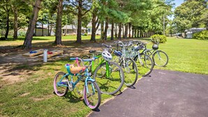 Eine Reihe von Fahrrädern, abgestellt auf einem befestigten Weg in einem Park, mit Bäumen und Häusern im Hintergrund.