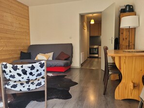 Uma sala de estar acolhedora com sofá, tapete de couro, mesa de jantar de madeira e cozinha ao fundo.