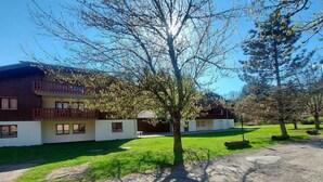 A two-story building with a balcony, a grassy lawn, and trees. - Studio with mountain views and pools, pets allowed (Samoëns)