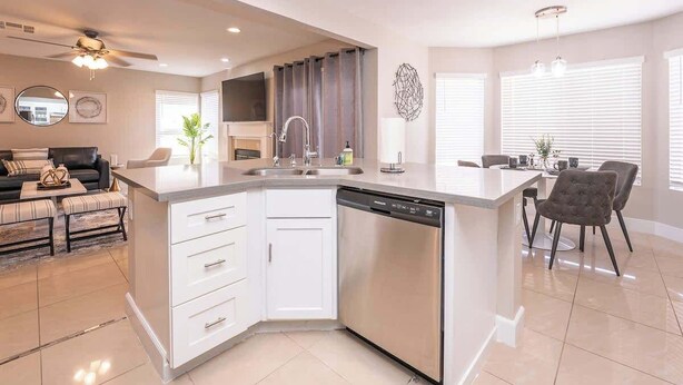 A modern kitchen with a dishwasher, a dining area with a table and chairs, and a living area with a sofa and a coffee table. - New Pool/Spa & Pool Table @ 6BR Refined Vegas Stay (North Las Vegas)