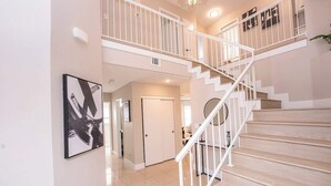 A spacious interior with a staircase leading to an upper level, a framed abstract painting, and a door leading to another room. - New Pool/Spa & Pool Table @ 6BR Refined Vegas Stay (North Las Vegas)