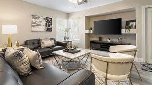 Un salon moderne comprenant un canapé, une table basse et un fauteuil, un téléviseur à écran plat et un ventilateur de plafond.
