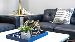 Un salon moderne avec une table basse bleue, un canapé en cuir noir et une plante décorative.
