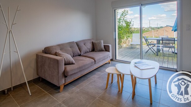 A modern living room with a sofa, two small tables, and a large sliding glass door leading to an outdoor patio.
