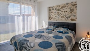 A bedroom with a large bed, a view of the outdoors, a stone wall, and a logo on the floor.