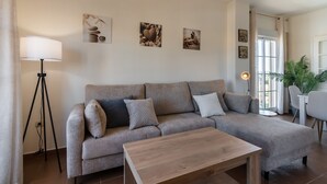 Un salon avec un canapé, une table basse et un lampadaire. On y trouve également des œuvres d’art murales et une plante.