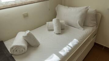 Een enkel bed met witte lakens, twee opgerolde handdoeken en een raam met gordijn.