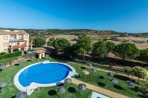 A swimming pool surrounded by lounge chairs and umbrellas, with a building in the background. - Albatros Golf I - Costa Esuri EAHGI173AP111 (Ayamonte)
