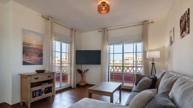 Un salon avec un canapé, un téléviseur, une table et un balcon offrant une vue agréable.