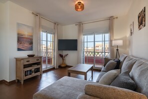 Un soggiorno con divano, televisore, tavolo e balcone con vista.