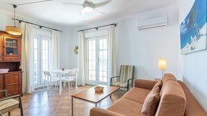 Una sala de estar con un sofá marrón, una mesa de comedor con sillas, un ventilador de techo y una ventana con cortinas.