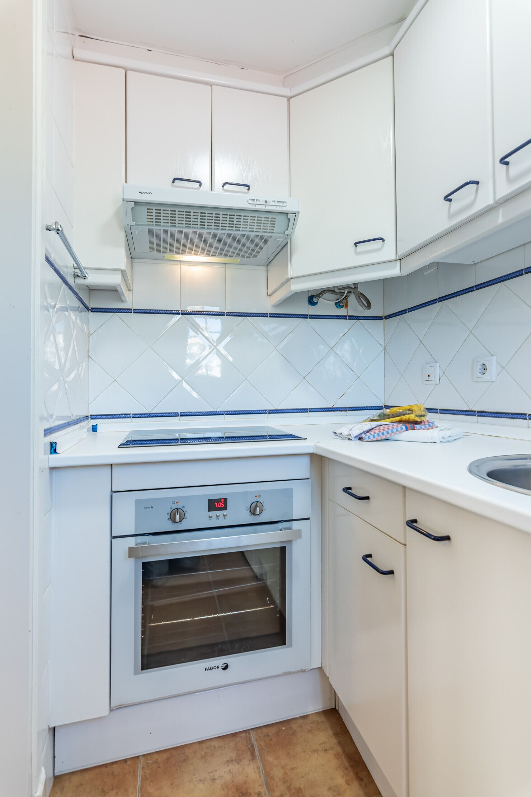 Eine kleine Küche mit weißen Schränken, einem eingebauten Backofen und einer gefliesten Spritzschutzwand.
