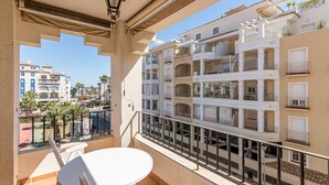 Un balcón con una mesa y sillas blancas, con vistas a una zona residencial con edificios altos y palmeras.