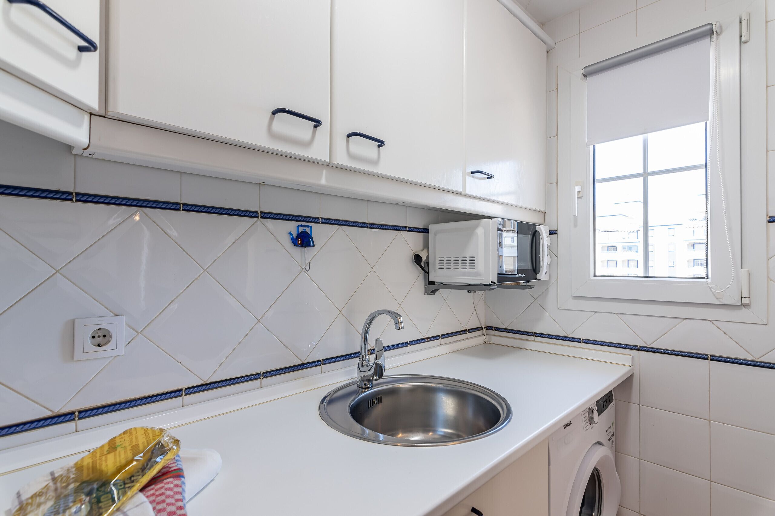 Une cuisine moderne avec des meubles blancs, un évier en acier inoxydable et un lave-linge encastré.