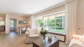 A spacious living room with a large window, a cozy sofa, a coffee table, and a dining area. - Reethüs - Keitum (Keitum)