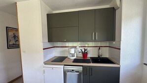 A compact kitchen with a dishwasher, a coffee maker, and a red cup holder.