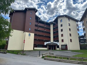 A multi-story residential building with a central entrance and a parking area in front.