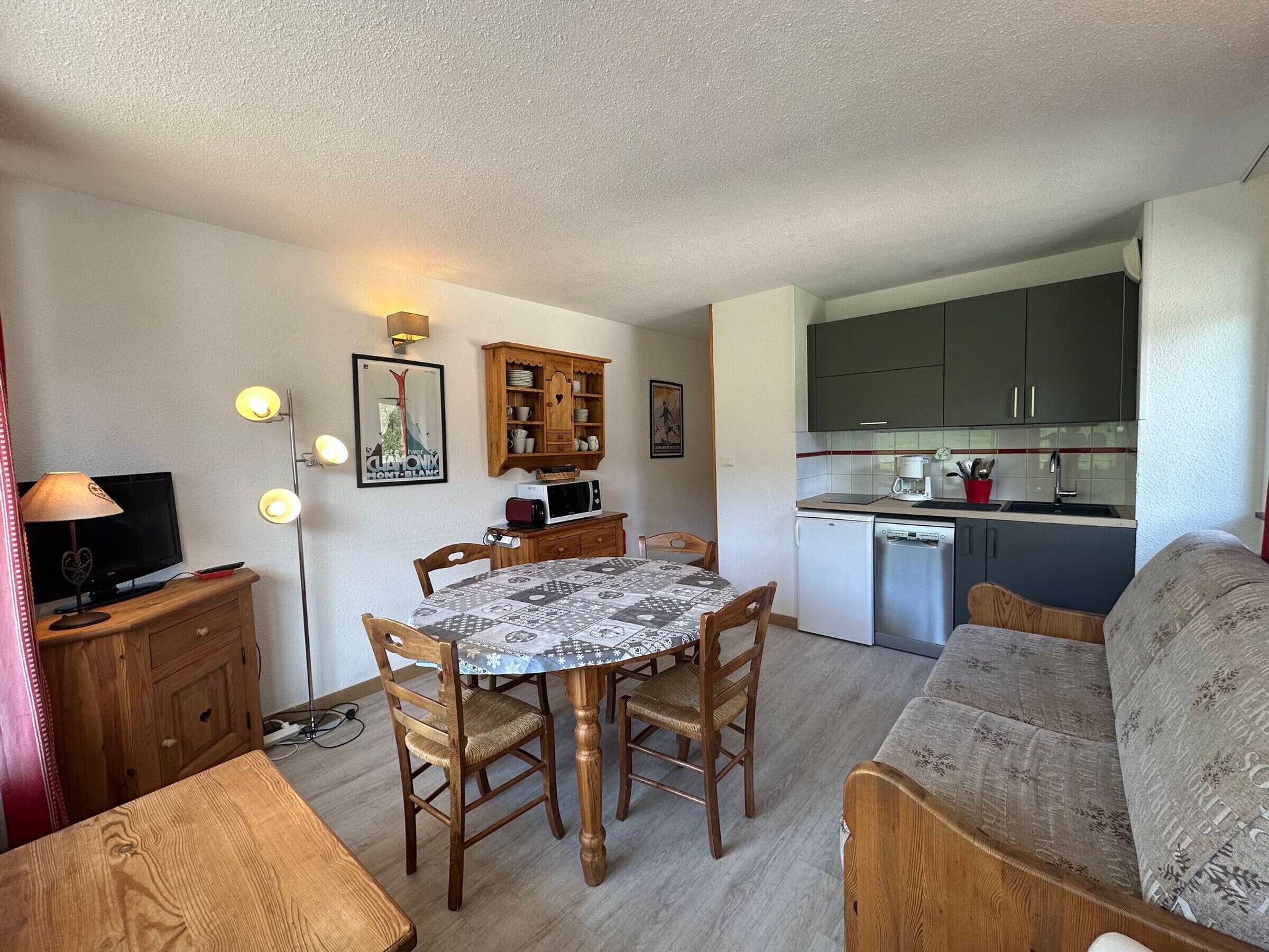 A compact living space with a dining table, chairs, a sofa, a kitchenette, and a television.